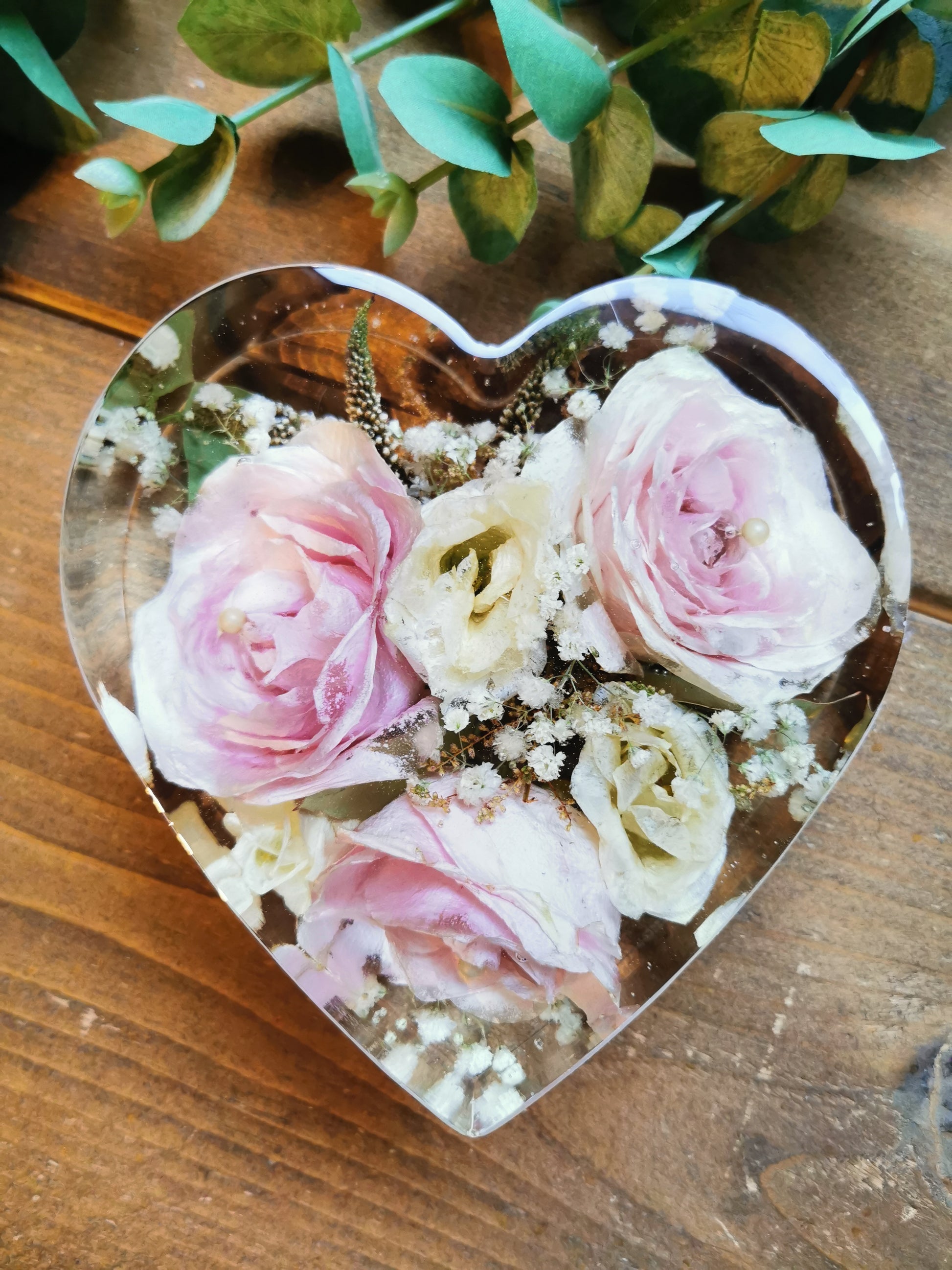 A clear freestanding heart-shaped resin piece filled with flowers, predominantly pink in color, arranged to form a floral heart display.
